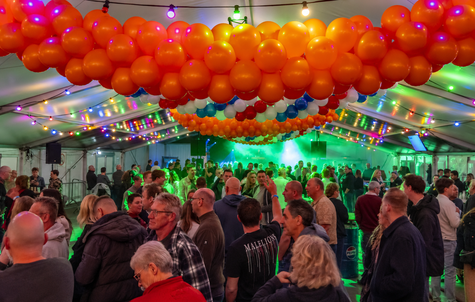 Feesttent met oranje ballonnenplafond en publiek